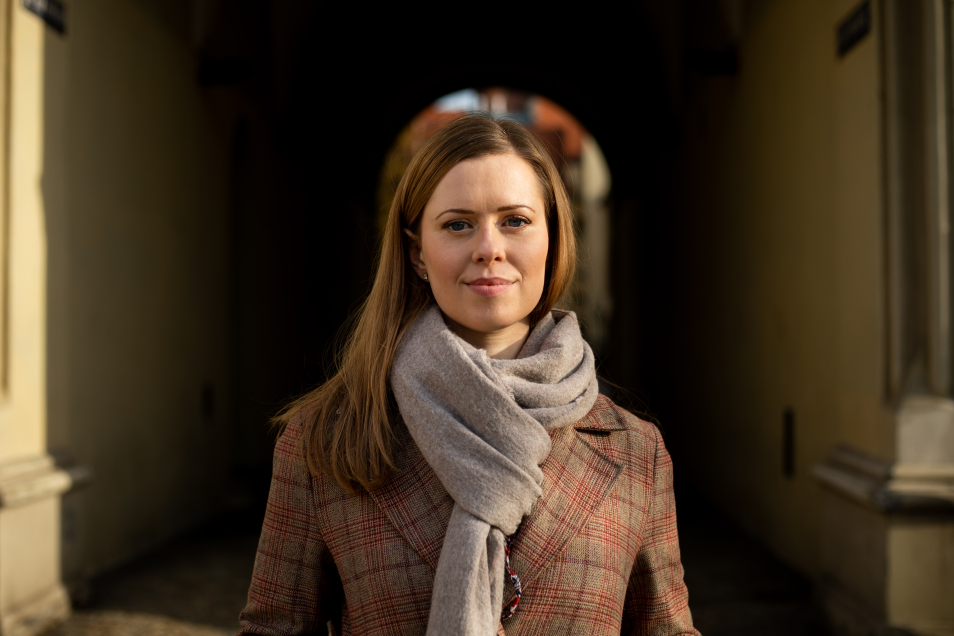Urszula Rybicka, w brązowym płaszczu i popielatym szalu, stoi pod arkadami kamienicy na rynku wrocławskim