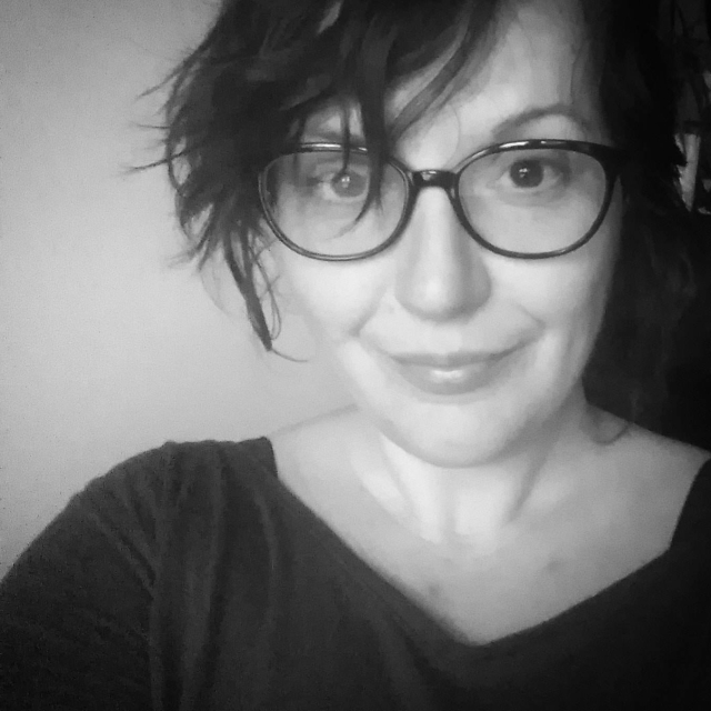 Małgorzata Baka, brunetka w okularach, uśmiecha się.