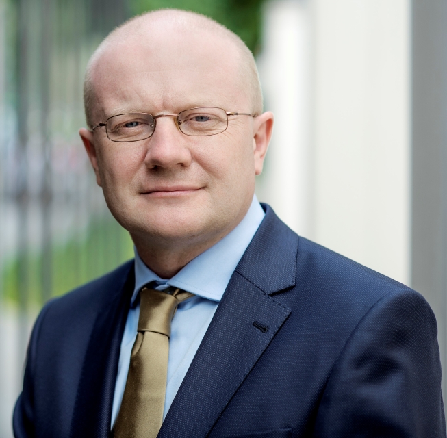 Maciej Duszczyk. Łysy mężczyzna w okularach i garniturze, ma także krawat.