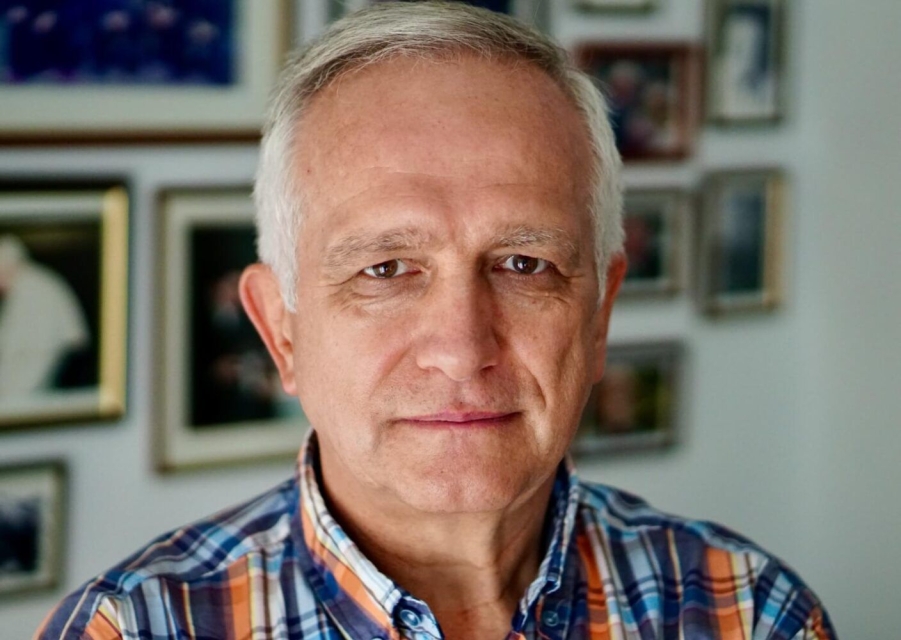 Zbigniew Nosowski - portret, ubrany w koszulę w kratę. W tle ściana z obrazami oprawionymi w złote ramy.