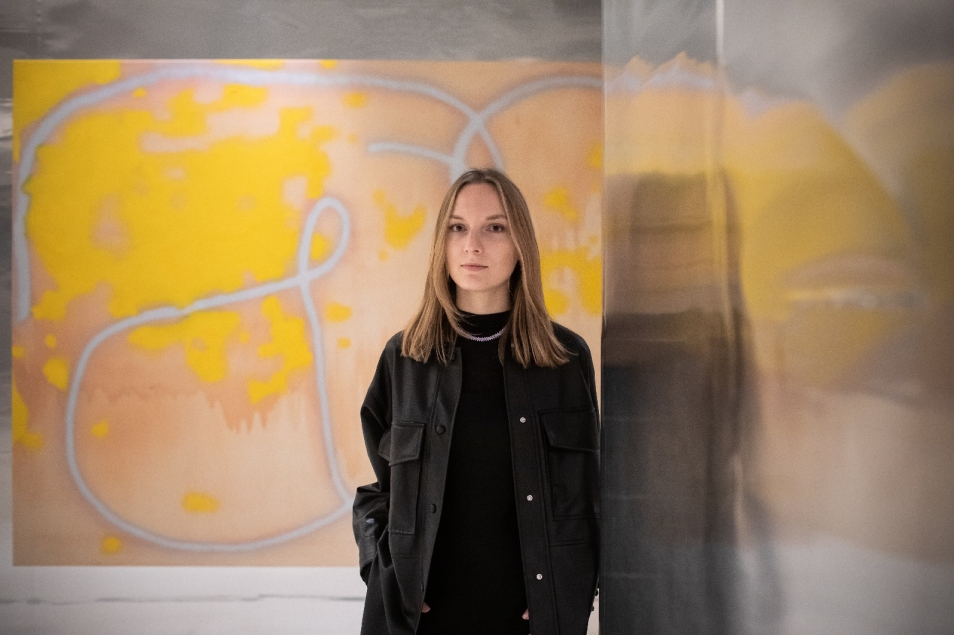 Marta Romankiv. Blondynka w ciemnym stroju na tle jednej z prac Wilhelma Sasnala.