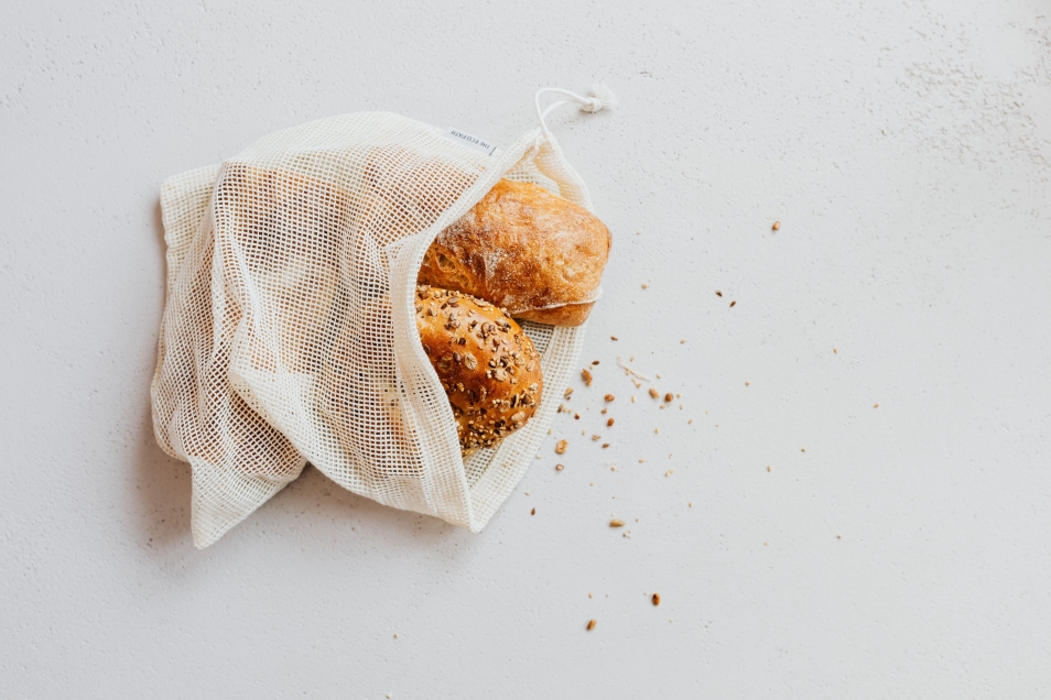 Dwie bułki z ziarenkami leżą w płóciennym woreczku.