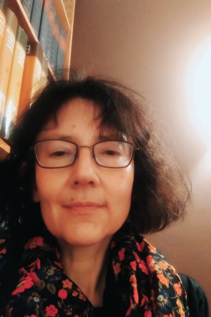 Katarzyna Stańczak-Wiślicz - krótko ścięta brunetka w okularach pozuje na tle biblioteczki.