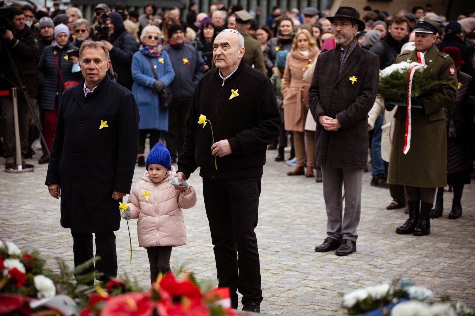 Zygmunt Stępiński i Piotr Wiślicki składają żonkile pod Pomnikiem Bohaterów Getta. Między nimi stoi mała dziewczynka.