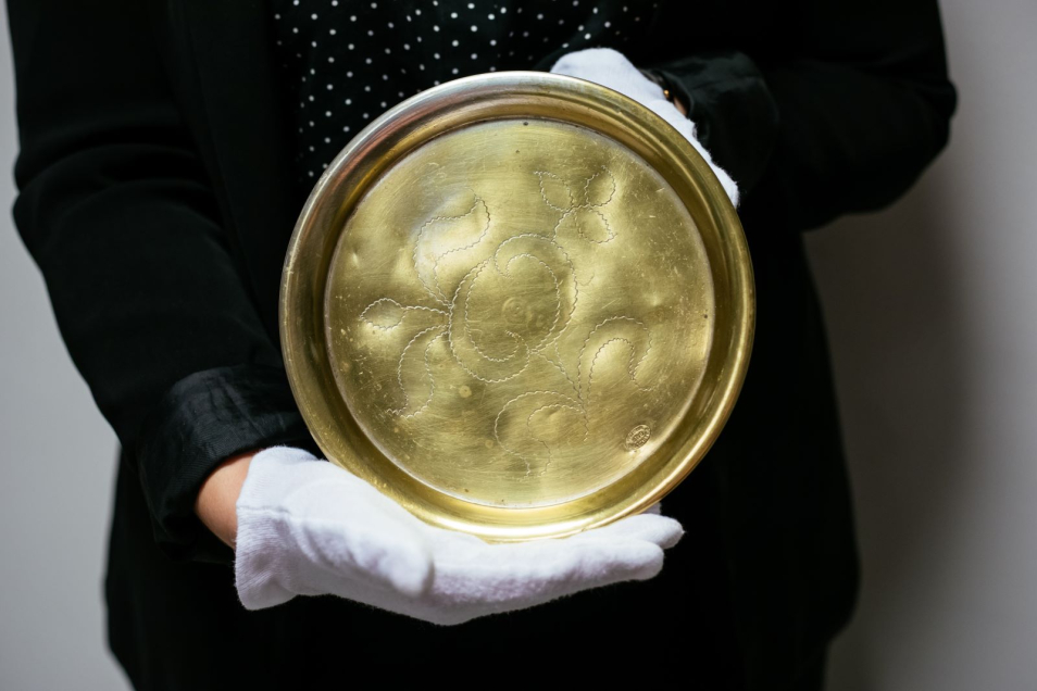 Osoba w białych rękawiczkach trzyma obiekt z kolekcji Muzeum POLIN - tacę z dekoracją floralną.