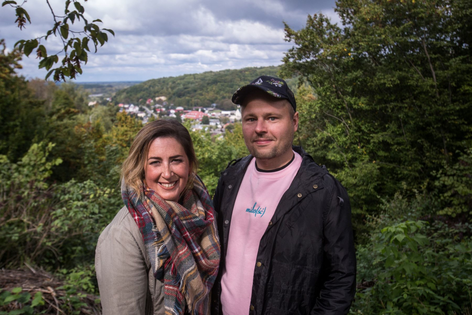 Mary i Radek stoją obok siebie na wzniesieniu. Za nimi las i jakieś domki.
