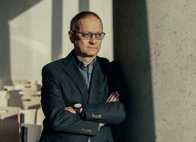Paweł Łuków stoi, opierając się o ścianę.