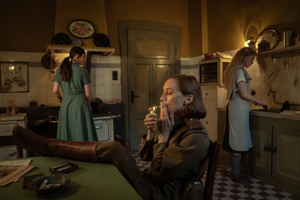 Kadr z filmu "Pociąg donikąd". W pomieszczeniu są trzy kobiety - dwie stoją, jedna siedzi z nogami założonymi na stole i pali papierosa.