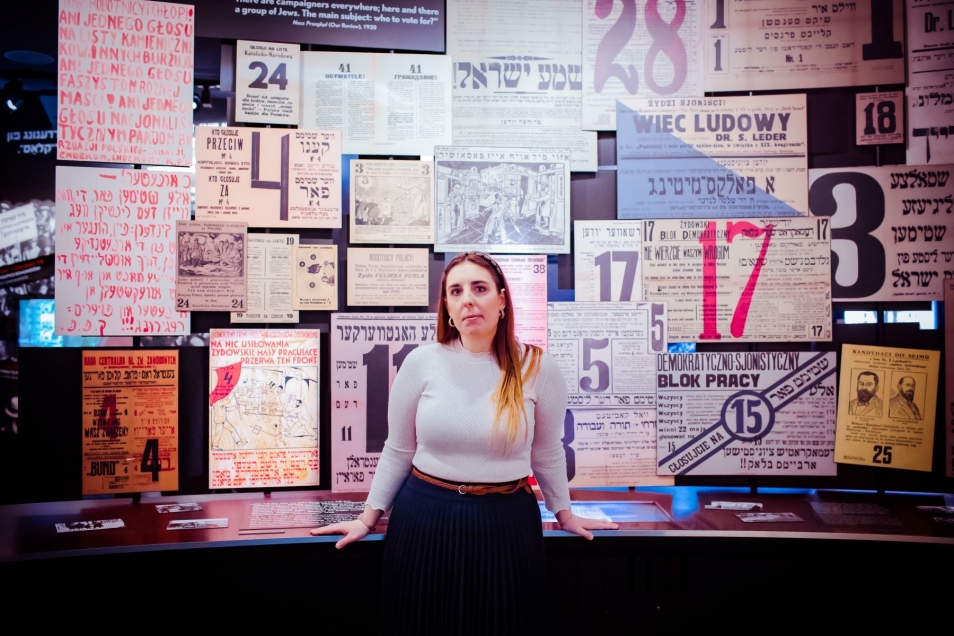 Katarzyna Jankowska - przewodniczka Muzeum POLIN - na wystawie stałej, przy plakatach propagandowych.