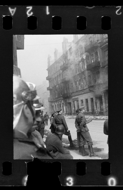Ulica Nowolipie, 1943. Podpalona kamienica w dzielnicy żydowskiej. Wokół stoją Niemcy i strażak w hełmie. EN: Polish firefighters and German soldiers observe burning buildings inside the Ghetto. 
