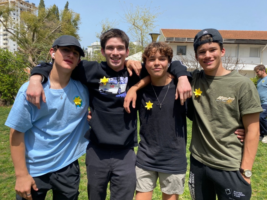 Sunny day in Israel. Four boys are standing next to each other. They are wearing paper daffodils on their clothes.