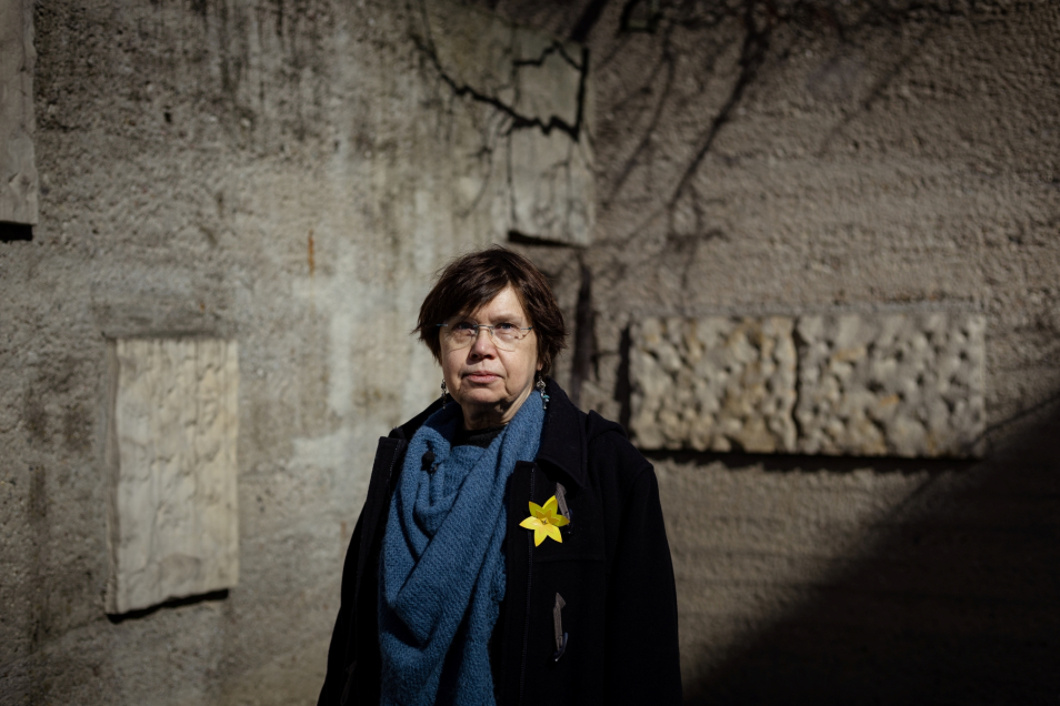 Profesor Barbara Engelking stoi na tle ściany bunkru. Do płaszcza ma przypięty papierowy żonkil.