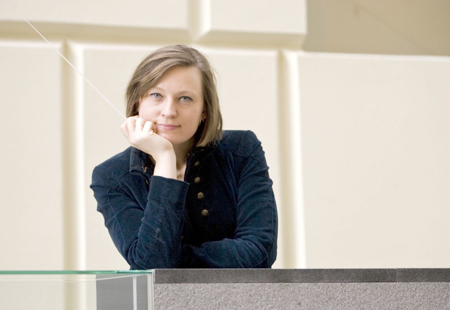 Anna Duczmal-Mróz opiera się o parapet. W dłoni, którą trzyma na twarzy, ma batutę.