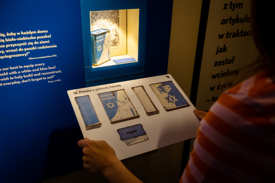 Kobieta trzyma przed sobą tyflografikę puszki z gwiazdą Dawida - eksponatu z wystawy stałej w Muzeum POLIN.