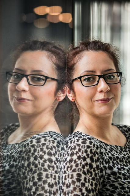 Paulina Małochleb stoi oparta o szybę, w której odbija się jej twarz.