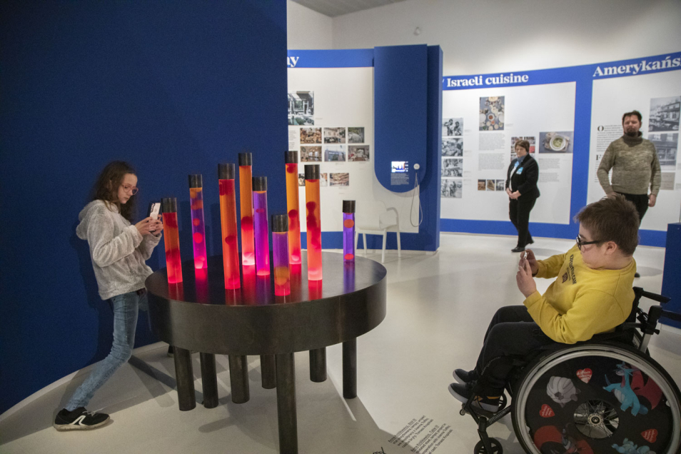 Dziewczyna i chłopiec - uczestnicy projektu fotograficznego - robią zdjęcia jednemu ze stołów na wystawie "Od kuchni"