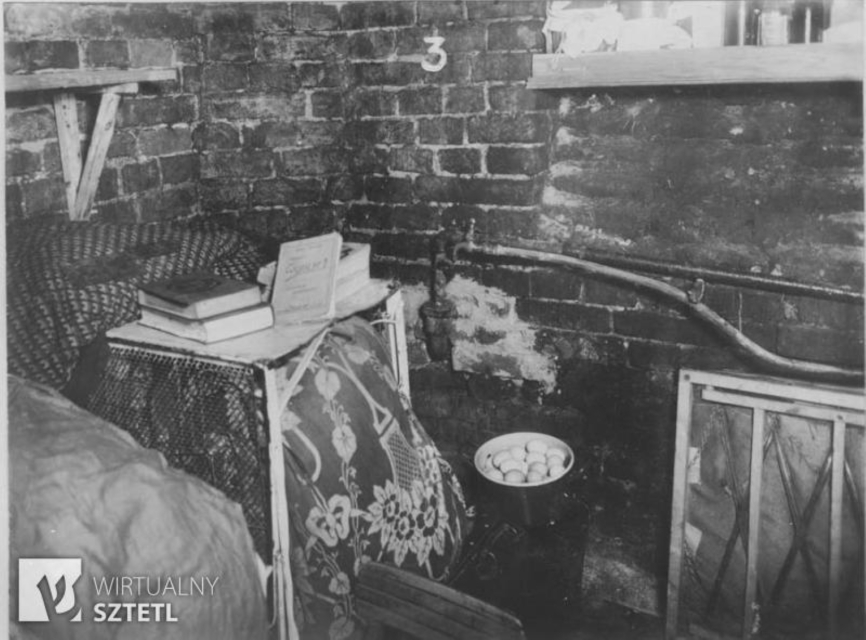 Інтер'єр криївки у Варшавському гетто під час повстання 1943 року. На столі лежать книги, внизу у відрі - яйця. Навколо мініатюрні меблі.