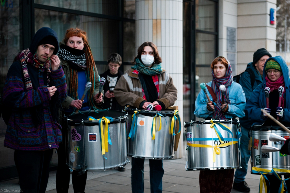 Aktywiści z grupy Samba Warszawski Rumor stoją z bębenkami przy jakimiś budynku w Warszawie.