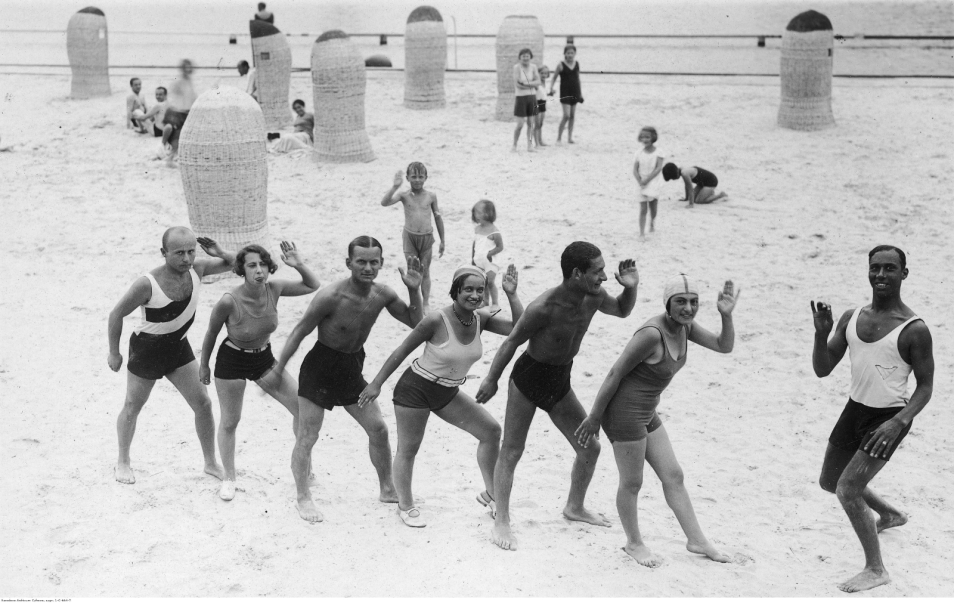 Grupa kuracjuszy podczas lekcji tańca na plaży prowadzonej przez czarnoskórego Sama z zespołu Kataszka.