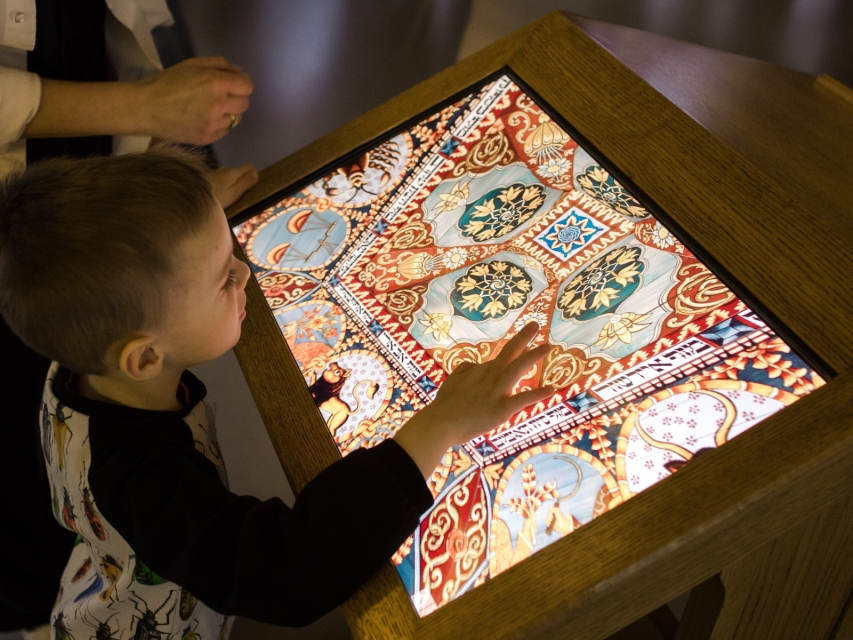 Chłopiec ogląda na ekranie multimedialnym zwierzęta znajdujące się na dachu synagogi z wystawy stałej Muzeum POLIN.