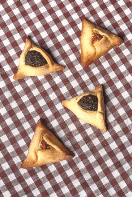 Cztery hamantasze leżą na kraciastym obrusie.