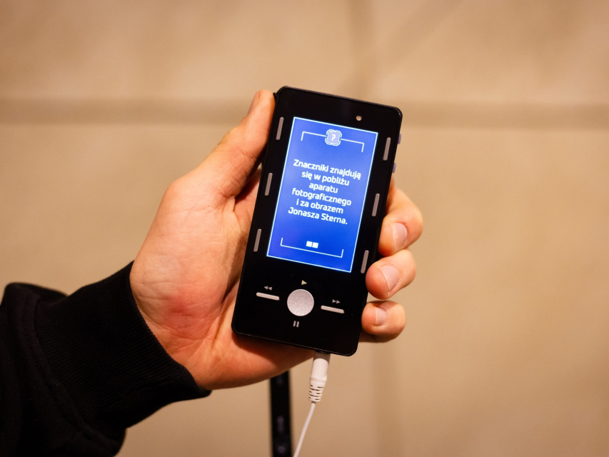 Ktoś trzyma przed sobą przenośny audioprzewodnik, który zawiera audiogrę dla młodzieży.