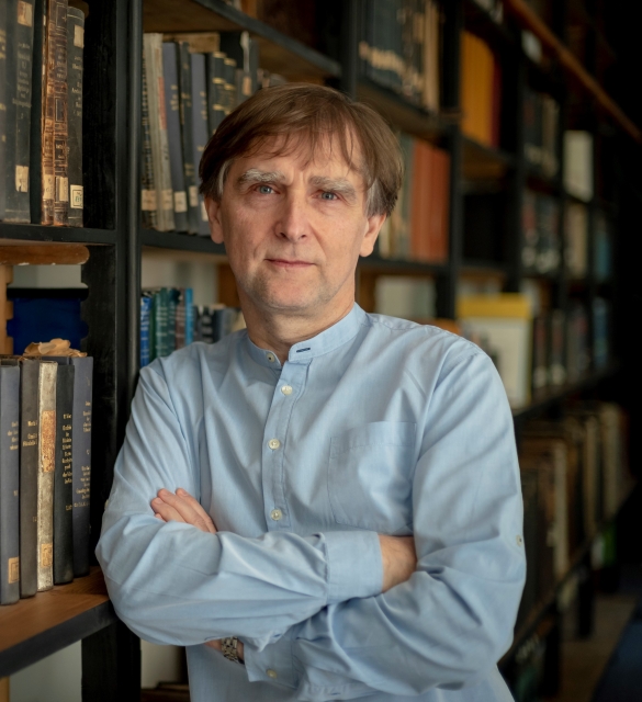 Marcin Wodziński stoi przy przeszklonej biblioteczce.
