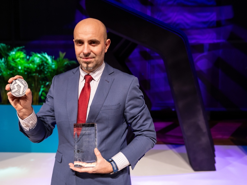 Mariusz Sokołowski trzyma w jednej dłoni medal okolicznościowy w drugiej - statuetkę za wygraną w konkursie Nagroda POLIN 2024.