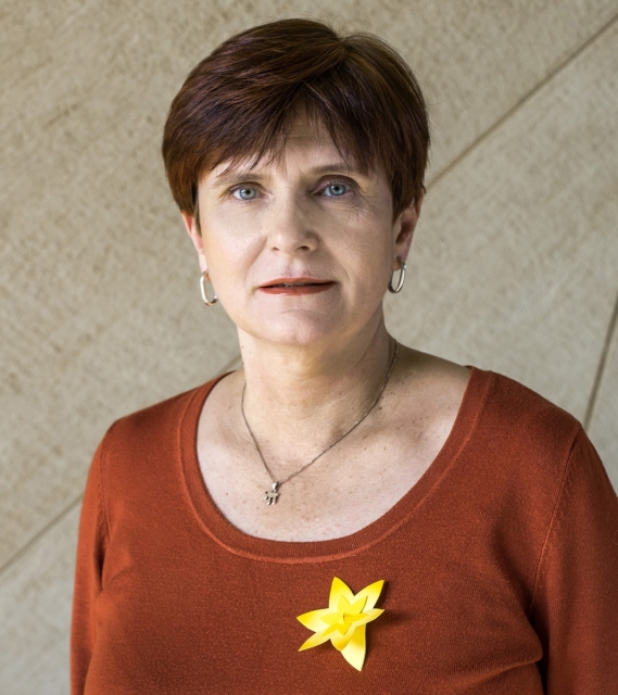 Monika Koszyńska na tle krzywoliniowej ściany w Muzeum POLIN. Do bluzki ma przypięty papierowy żonkil.