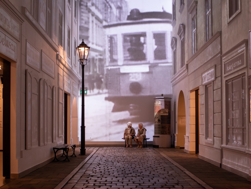 Seniorki siedzą na ławeczce w galerii "Na żydowskiej ulicy" na wystawie stałej.