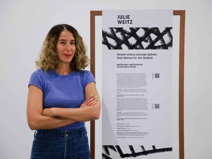 Julie Weitz na tle stojaka zawierającego opis jej performansu.