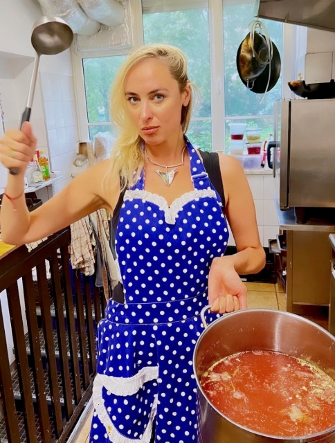 Maria Toboła w jednej dłoni trzyma chochlę, drugą podtrzymuje gar pełen zupy.