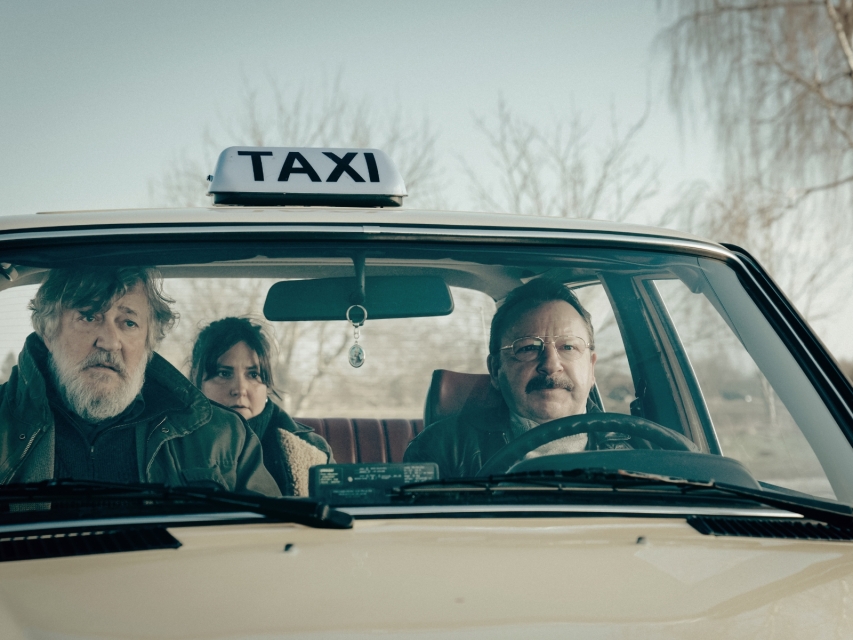 Kadr z filmu "Treasure" - trzy osoby jadą taksówką.