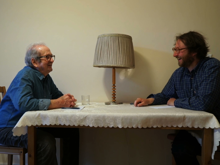 Kadr z filmu "Zamek mojego ojca". Ojciec i syn siedzą przy stole nakrytym obrusem.