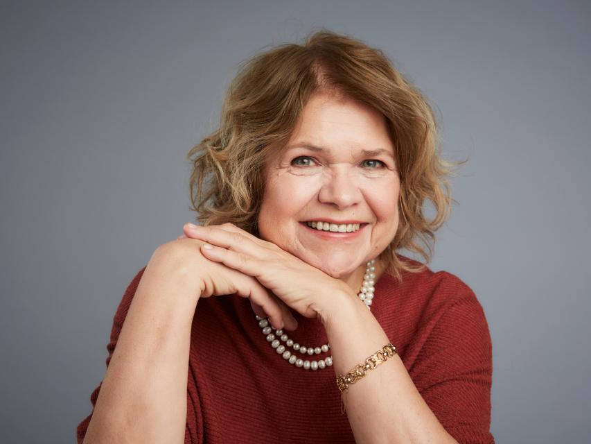 Anna Bikont - uśmiecha się i opiera obie dłonie na brodzie.