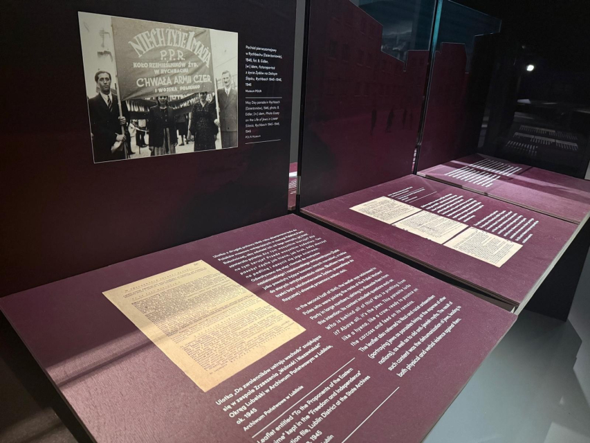 Przestrzeń wystawy "1945. Nie koniec, nie początek" - archiwalne zdjęcie czarno-białe z napisem "Niech żyje 1 maja" oraz pulpity z tekstami.