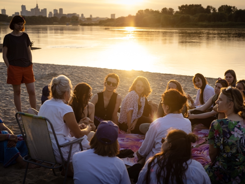 Grupa osób uczestnicząca w Muzealnym Think-tanku siedzi na plaży nad Wisłą w Warszawie.