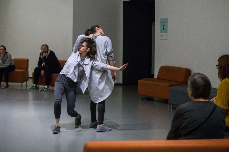 Two women in white shirts are standing with their backs to each other.