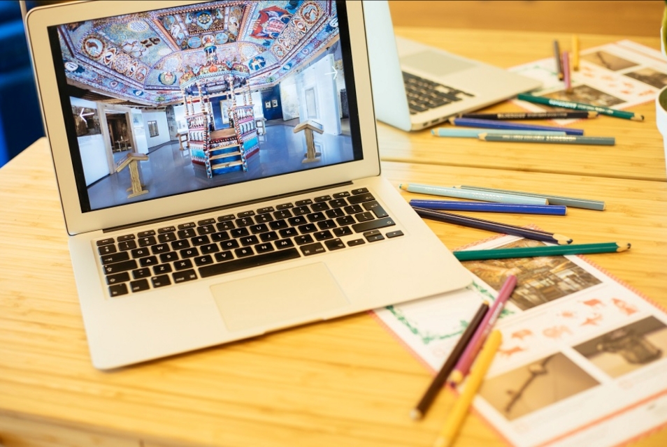 Na biurku rozrzucone kolorowe kartki i ołówki. Otwarty laptop, na którego ekranie widać rekonstrukcję dachu synagogi z Gwoźdźca.