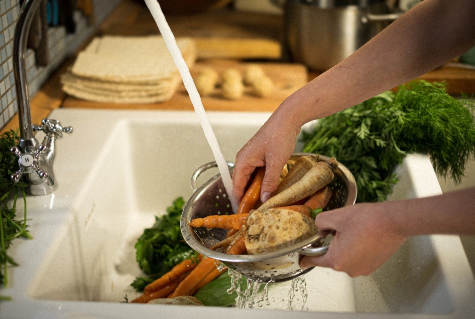 Someone is washing parsley, celery and carrots in a colander over the sink.