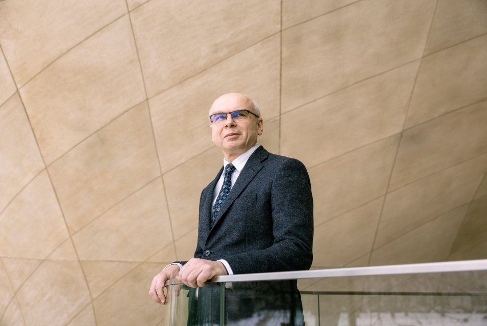 Dariusz Stola opiera się o balustradę w holu głównym Muzeum POLIN. Patrzy w bok.