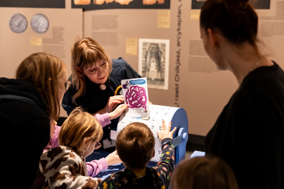 The educator shows the children and their carers a colourful picture at the exhibition The Power of Words: On Jewish Languages.