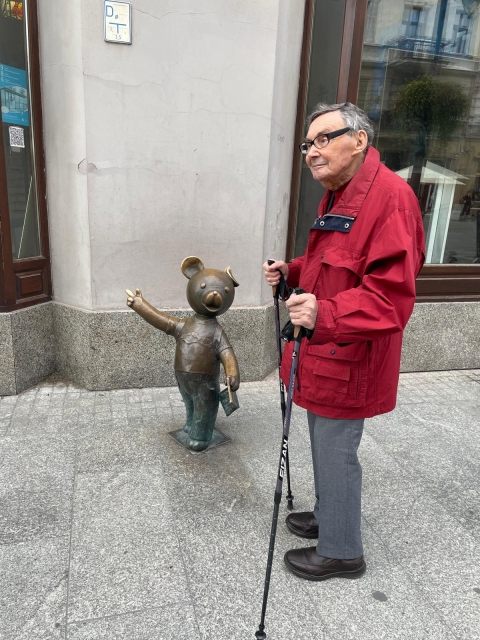 Marian Turski na ulicy w Łodzi. Stoi z kijkami przy pomniku Misia Uszatka.