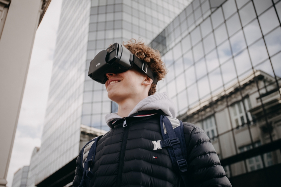 Nastolatek ma na głowie gogle VR. W tle Błękitny Wieżowiec na placu Bankowym w Warszawie.