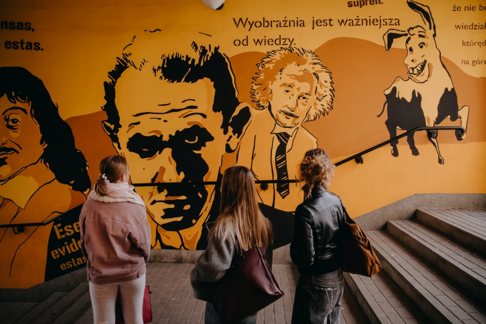 Trzy nastoletnie dziewczyny oglądają mural w podziemiu. Jedną z namalowanych postaci jest Albert Einstein.