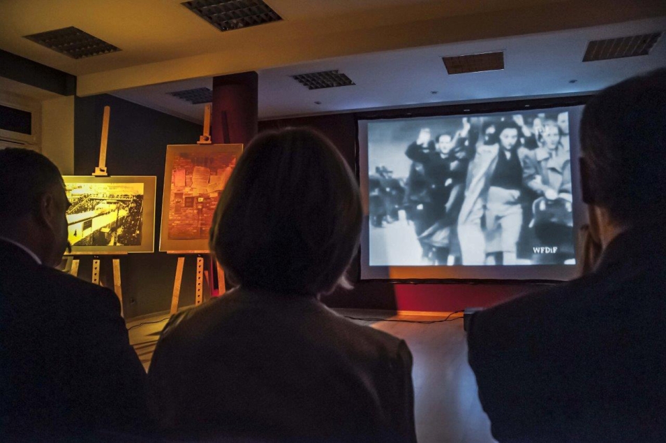 Kilka osób ogląda film wyświetlany na ekranie.