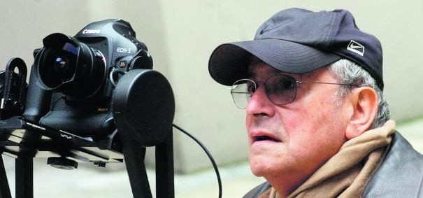 Fotograf w czapce z daszkiem stoi przy aparacie umieszczonym na statywie.