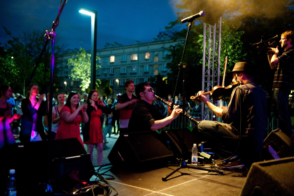 Koncert nocą w okolicach Muzeum POLIN. Grupa muzyków gra na instrumentach.