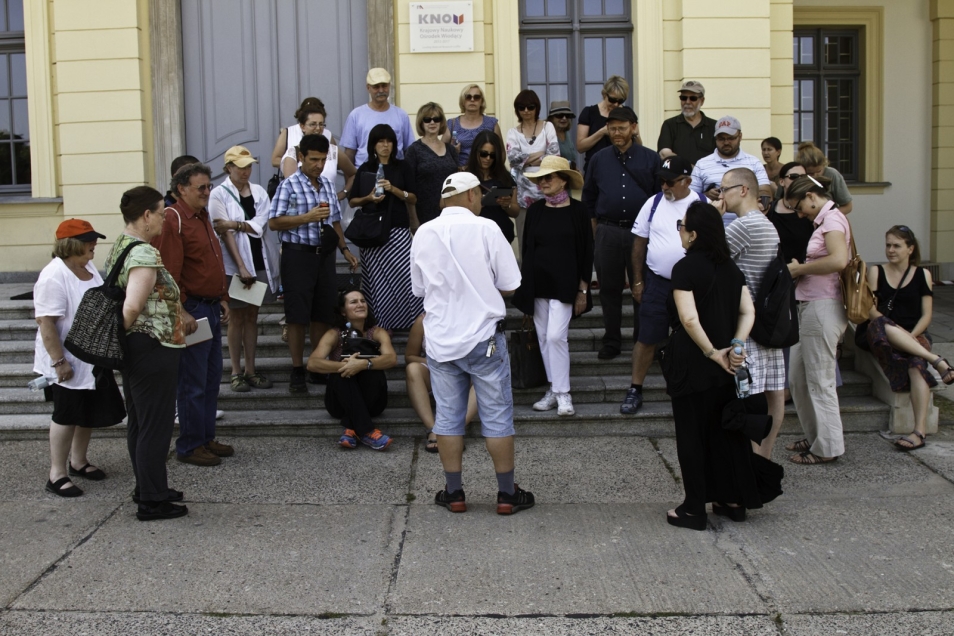 Grupa osób siedzi lub stoi na schodkach przed budynkiem.