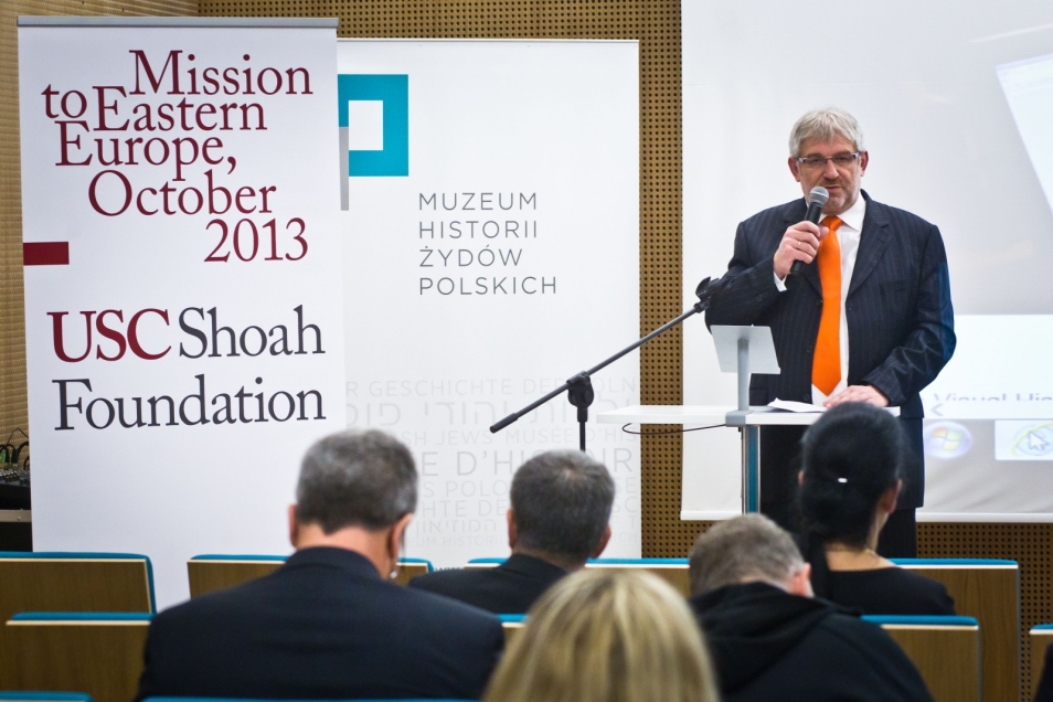 Mężczyzna w garniturze mówi przez mikrofon podczas konferencji USC Shoah Foundation w 2013 r.
